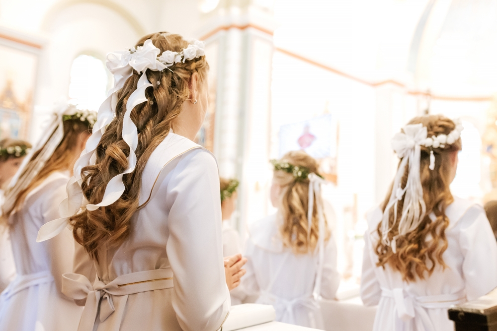 Dziewczynki podczas uroczystości I Komunii świętej, w długich włosach, jasnych szatach i białych wiankach